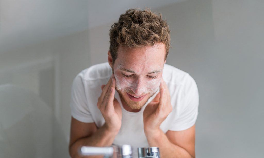 Man washing face with facial cleanser face wash soap in bathroom
